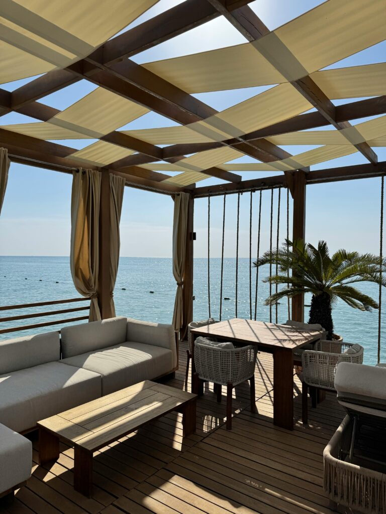 Elegant beachfront outdoor lounge under a pergola with ocean view.