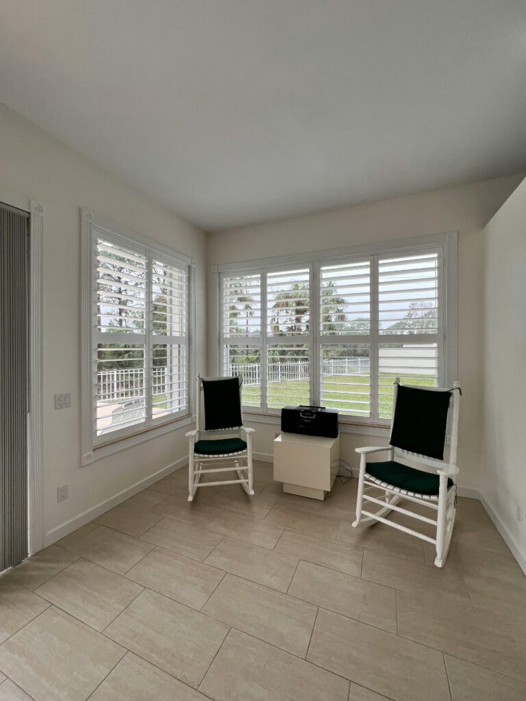 Cozy sunroom with plantation shutters, two chairs, and outdoor view.