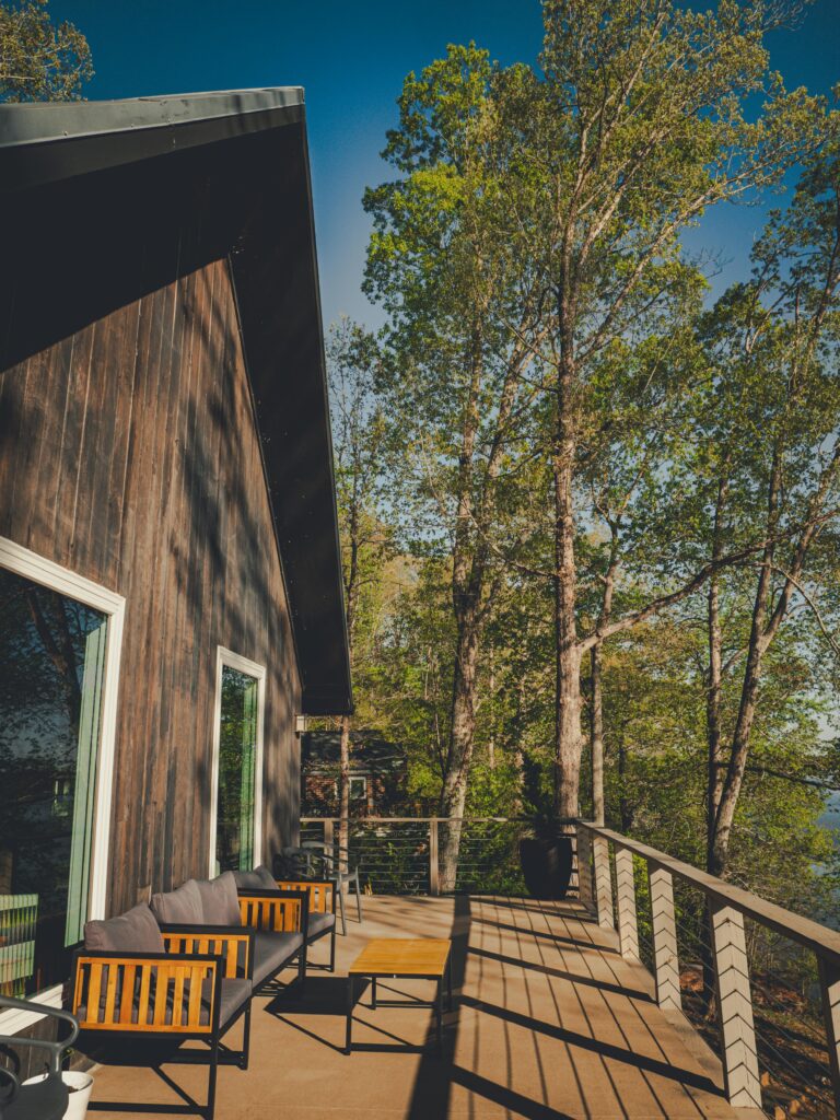A modern cabin with a sunlit deck overlooking lush green forest trees, evoking a serene outdoor retreat.