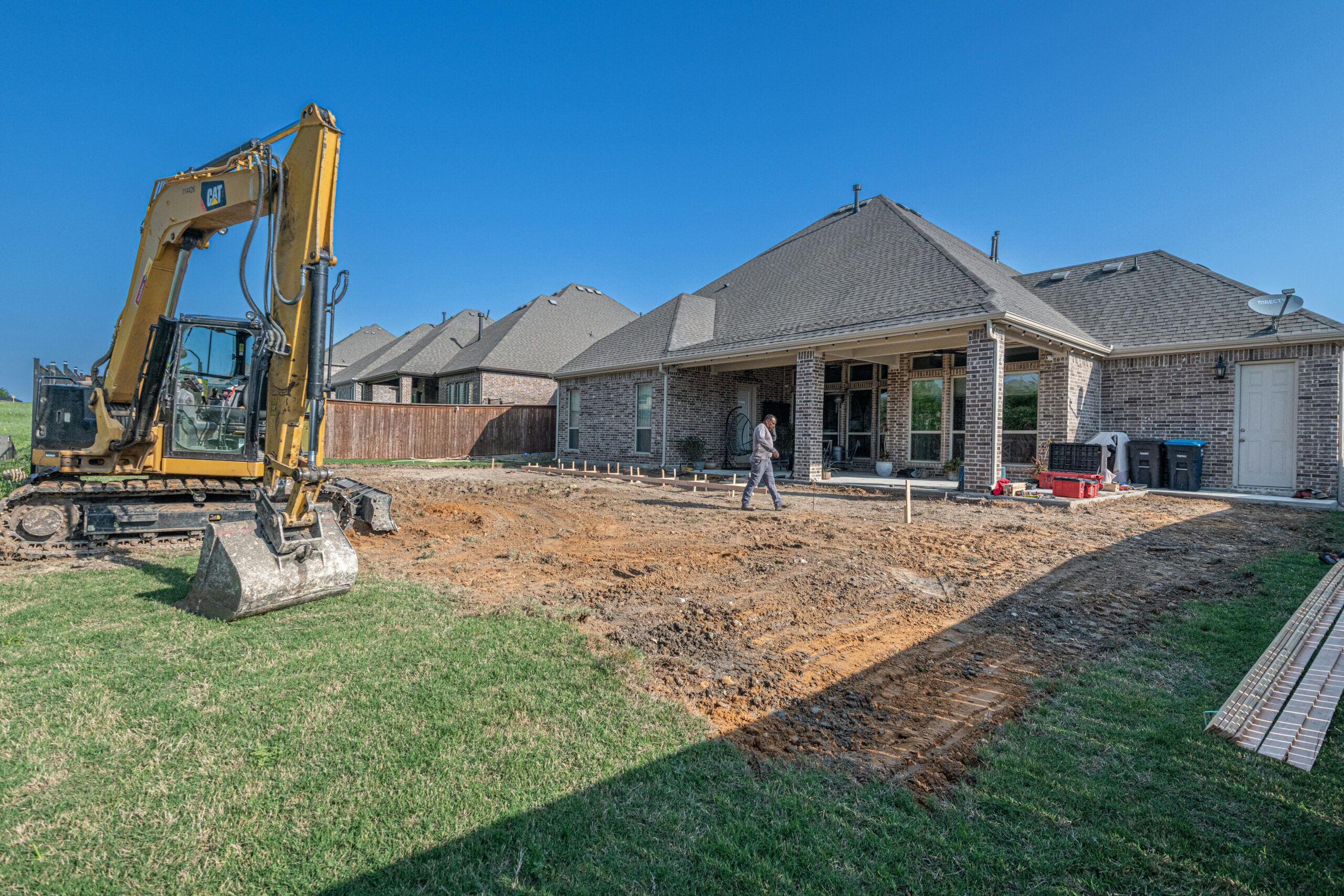 A construction site for a new patio in a Texas backyard with heavy machinery.